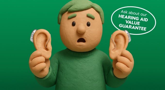 Claymation figure with hearing aids holds two large ears; speech bubble reads, Ask about our hearing aid value guarantee, on a green background.