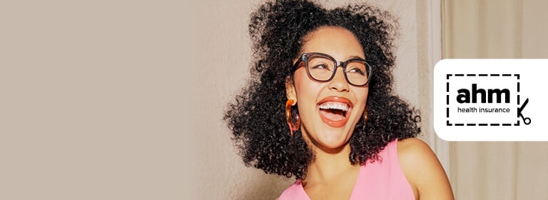 A person with curly hair and glasses is smiling. ahm health insurance logo.