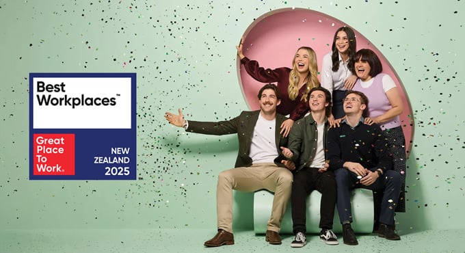 Five professionally dressed people pose in front of a green background next to a Best Workplaces New Zealand 2025 sign from Great Place to Work.